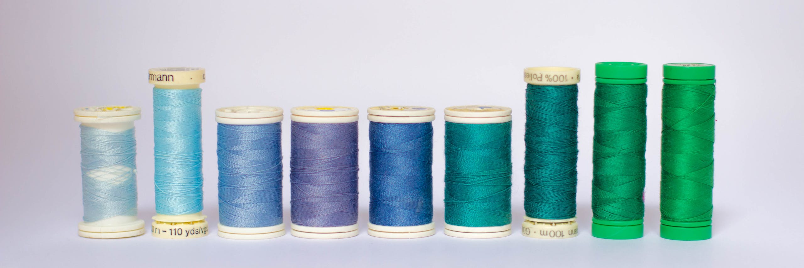 A variety of blue and green sewing thread spools arranged on a white background.
